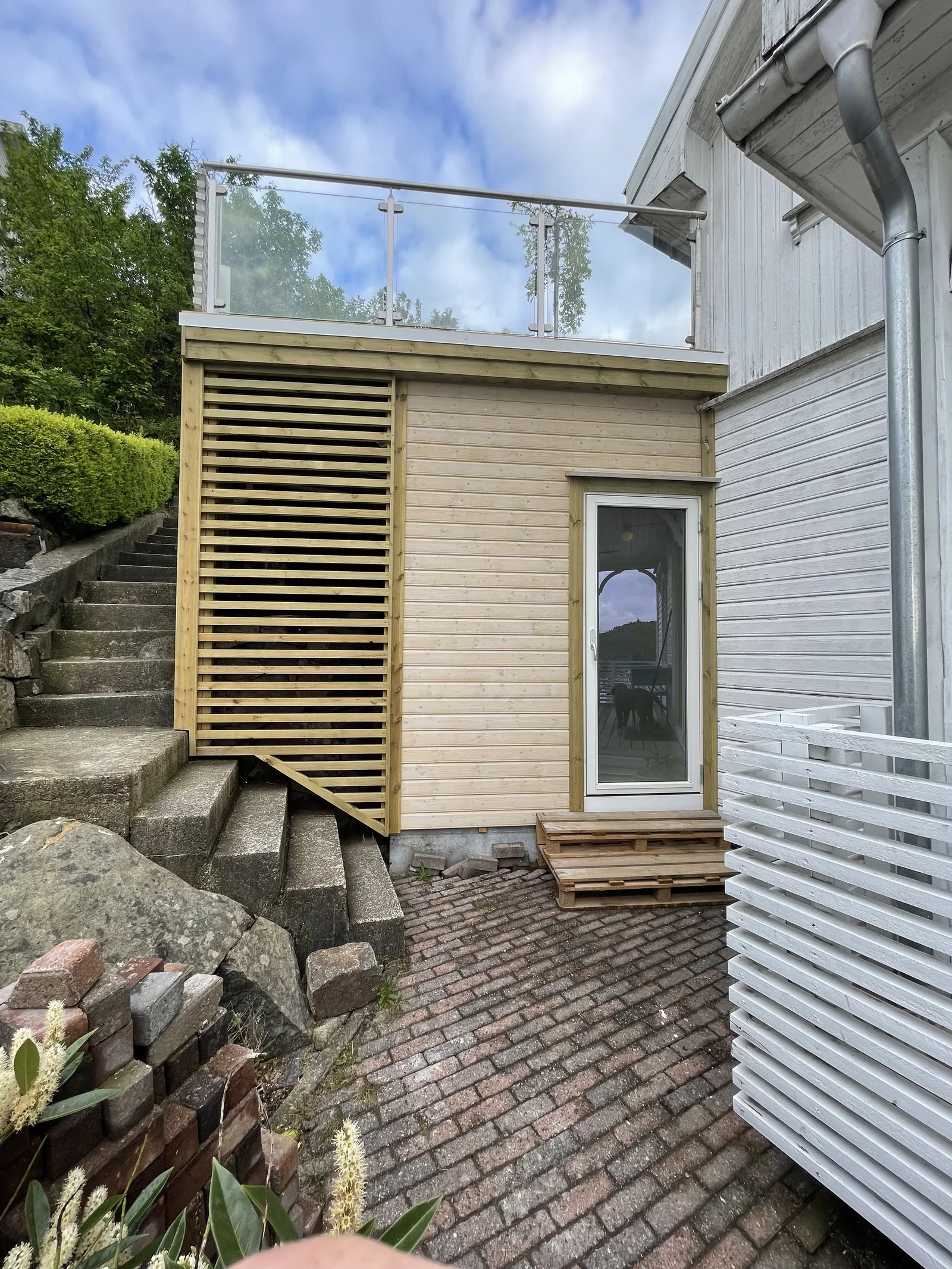Lyst trekledd volum med takterrasse inntil et hvitt hus.