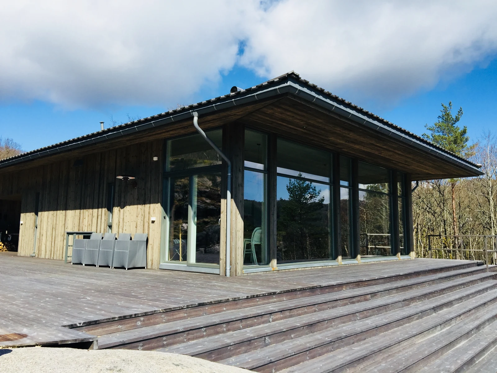 Trehytte med store glassflater, overbygd terrasse og brede tretrinn. Foto fra Hansen Bygg.